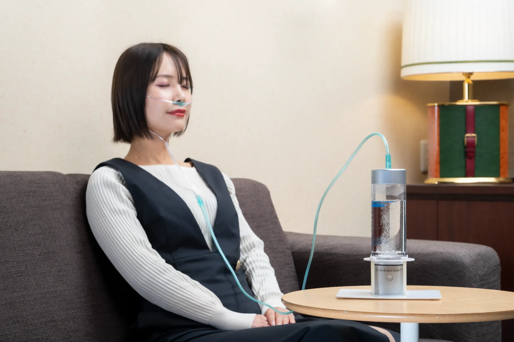 ソファでドクター水素ボトル+の水素ガスを吸入する女性